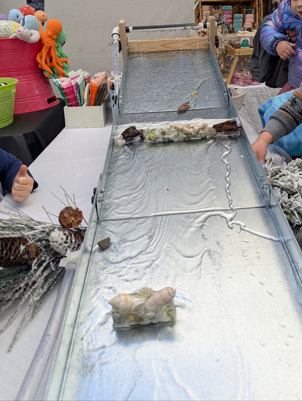 Children and a woman at a table with a epoxy display case containing small objects.